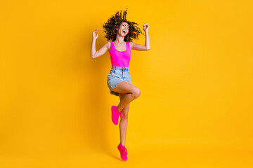 Fototapeta na wymiar Full length photo of charming amazing curly lady jump up high students party delighted rejoice wear pink tank top denim mini skirt shoes isolated vivid bright yellow color background