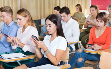 Group of modern people sitting with mobile phones on lecture in the classroom