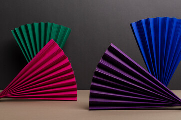 Closeup of colorful paper fans on the beige background against dark grey wall.Empty space