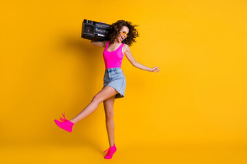 Fototapeta na wymiar Full size photo of cool attractive lady listen music hold shoulder retro boom box chill students party event wear sun specs pink singlet denim skirt shoes isolated yellow color background