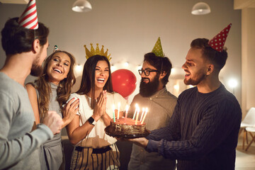 Group of friends giving birthday cake to happy woman during party at home, in cafe or restaurant