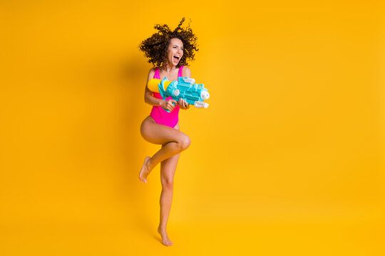 Photo portrait of woman holding water gun standing on one leg wearing pink swim wear isolated on vivid yellow colored background