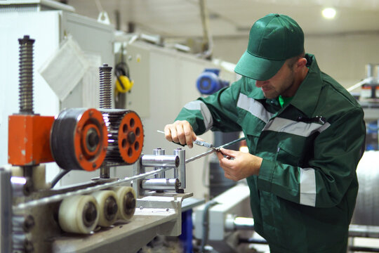 factory worker in a robe and cap checks the performance of the device for the production of cable products from a copper core