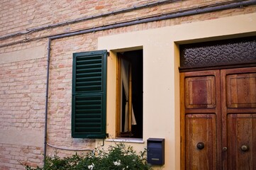A facade of an old traditional italian house with an open window and a wooden door (Corinaldo, Italy, Europe)