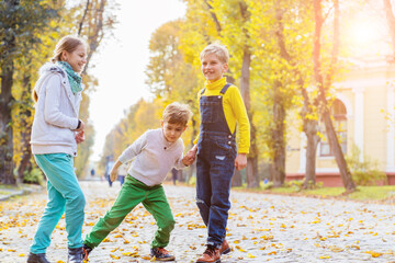 Fototapeta premium Children girl and two boys playing with soap bubbles, someone blows children catch bubbles. Beautiful natural landscape, autumn park on background, happy childhood.