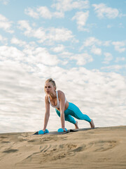 Fototapeta na wymiar Young blonde woman doing workout outdoors on the sand. Modern healthy lifestyle.