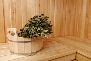 Dry bath broom lying in a round wooden bucket standing on a bench in the sauna