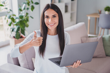 Photo of approving charming young brunette woman show thumb up hold laptop home freelancer inside...