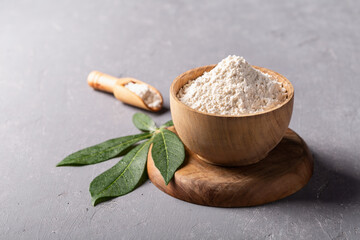 Cassava flour in wooden bowl with original leaf on grey background.
