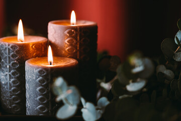 Black burning candles against dark red background with eucalyptus branch.