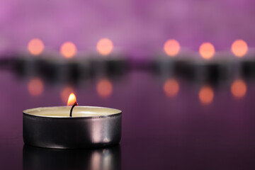 A small glowing candle on the background of a group of candles.