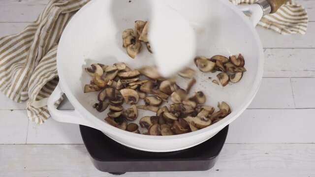 Sauteed organic baby bella mushrooms in a white frying pan.