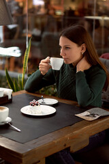 young woman drinking coffee in a cafe and eating dessert