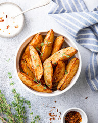 baked potato wedges with paprika, thyme and sauce on a light background, top view