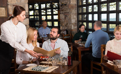 Fototapeta na wymiar Guests of the country restaurant discuss menu with waitress. High quality photo