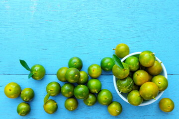 Yellow green calamansi, calamondin or philippine lime tropical fruit pattern in bright blue wood background. Asian summer citrus fruits flat lay composition.