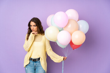 Young woman catching many balloons over isolated on purple background thinking an idea