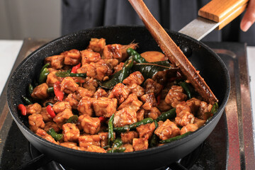 Making/Sauteeing  Orek Tempe, Indonesian Cuisine Made from Cubed Tempeh with Spice, Chilli, and Sweet Soy Sauce. Using Wooden Spatula, Home Cooking Process in the Kitchen