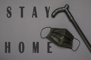 StayHome words on the grey surface.Top view of black walking cane and facial mask 