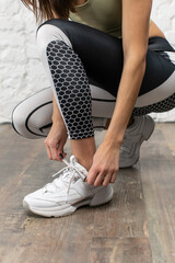 Cropped close up photo of sporty woman in sportswear ties the laces on her white sneakers before training in gym