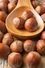 Top view of hazelnuts in wooden spoon and on rustic table, with selective focus, vertical