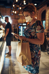 Young woman shopping in grocery store in the evening, wearing the face mask to avoid virus infection and to prevent the spread of disease in time of coronavirus