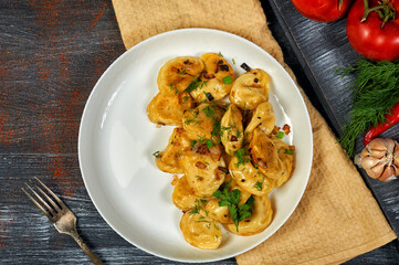 Fried traditional dumplings stuffed with potatoes and meat, sprinkled with bacon cracklings and chopped parsley on a white plate on a rustic table, top view.