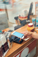 Woman paying for medicines at pharmacy using contactless method of payment via mobile phone. Woman using new way of payments