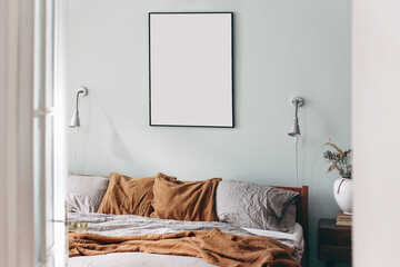 Portrait black picture frame mockup on sage green wall. Bedroom view through open white door. Grey linen and rusty muslin pillows on wooden bed. Scandinavian interior. Ceramic vase with dry grass.