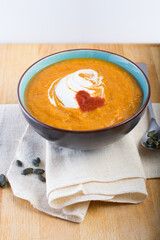 An orange pumpkin soup in a bowl on a linen cloth with pumpkin seeds and a spoon