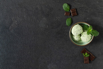 Scoops of mint ice cream with chocolate crumbs in a plate on black background top view. © Inna Dodor