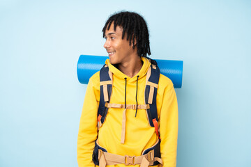 Young mountaineer african american man with a big backpack isolated on a blue background looking to the side
