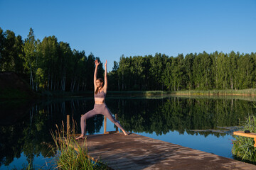 Young Woman practicing yoga on the wooden berth at lake. Single sport healthy training on nature at sunny weather