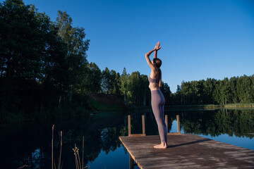 Fototapeta na wymiar Girl is practicing yoga technique on the pier by the lake and meditating. Meditation to purify mind and calm.