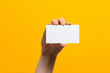 Raised female hand with a white card. Mock up. Yellow background. Copy space