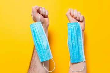 Female's and male's hands hold medical masks in their fists. Yellow background. Concept of protection against coronavirus and other diseases