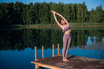 Fototapeta na wymiar Woman doing yoga on a forest lake. Beautiful girl doing exercises on stretching and flexibility outdoors