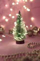Close-up view of a decorative live mini-Christmas tree in a soft bokeh of garlands of lights