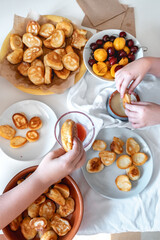 Delicious breakfast with tiny mini pancakes, cherries, apricots, jam on a white table. Small children hold pancakes in their hands. view from above