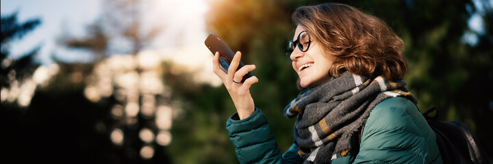 Young beautiful curly happy woman in glasses in a jacket and a scarf talking chatting mobile phone...