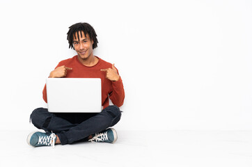 Young african american man sitting on the floor and working with his laptop with surprise facial expression