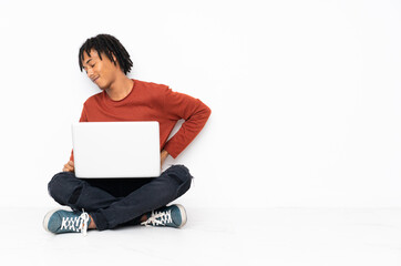 Young african american man sitting on the floor and working with his laptop suffering from backache for having made an effort