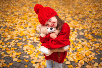 Happy little girl playing with his teddy bear toy in autumnal park