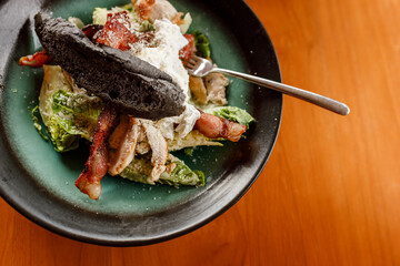 Caesar salad with chicken, romaine lettuce, cherry tomatoes, avocado, bacon, parmesan on wooden table