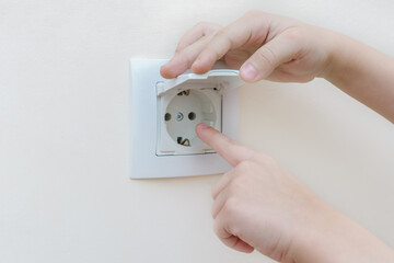 close-up of children's hands trying to stick a finger into the socket. Idea - danger for children in the house, teaching children about safety. Horizontal photo