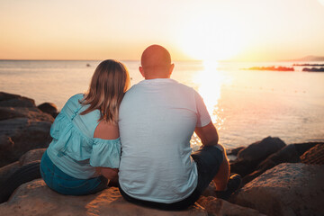 An adult couple, a plus-size man and woman, sit on the beach, watching the sunset over the ocean. Rear view. The concept of Valentine's day