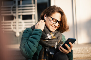 Young woman with wireless headphones and mobile device listening to music outdoor in city