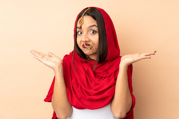 Young Indian woman isolated on beige background making doubts gesture