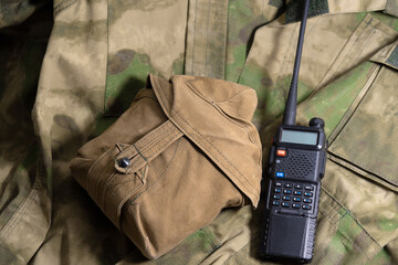 a black handheld radio lies next to the flask on a military camouflage jacket