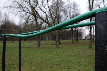 Fototapeta premium Empty old bent metal gymnastic bars close up on an abandoned sports field in the Park on a cloudy autumn day on green grass and bare trees background